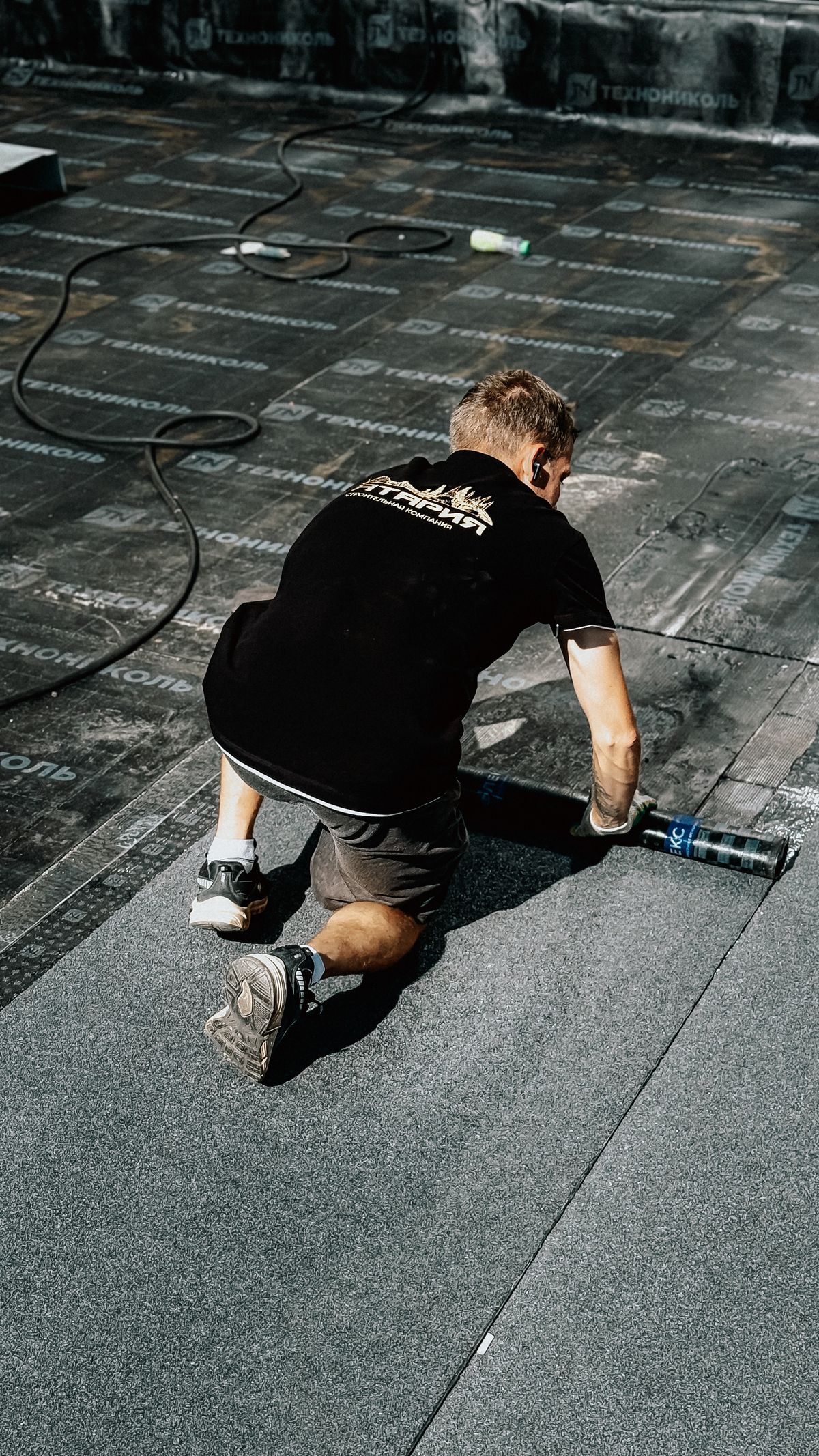 A worker preparing rolled roofing on a low-slope roof